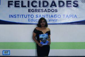 joven graduada sonriente con diploma frente al banner de felicitaciones del Instituto Santiago Tapia.