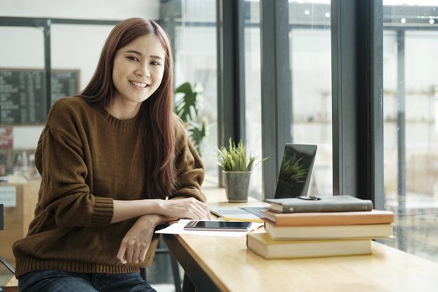 Mujer joven estudia con libros y tablet en un ambiente moderno y acogedor.