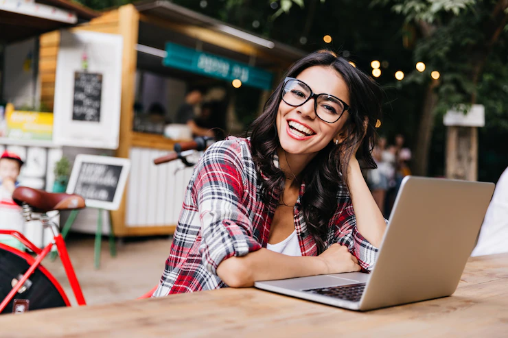 Mujer sonriente trabaja con laptop en ambiente acogedor al aire libre.